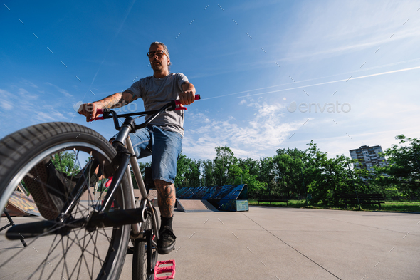 Low angle view of an active mature tattooed man practicing bike tricks in a skate park.