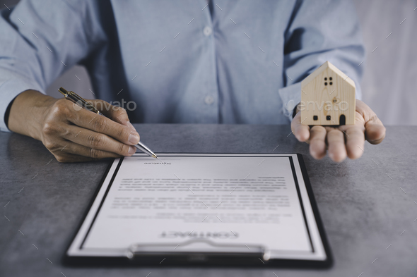 Real estate agent holding home and signing contract about agreement of real property on desk, house