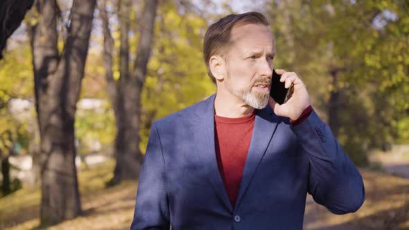 A Middleaged Handsome Caucasian Man Talks on a Smartphone As He Walks in a Park in Fall