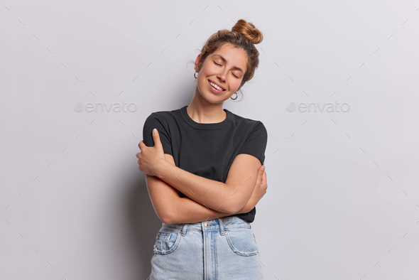 European girl in black t shirt embraces herself in sweet self hug isolated on white background