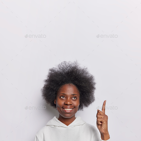 Joyful female model with curly hair directs attention to captivating advertisement above presenting
