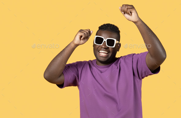 Happy African Man Wearing Sunglasses Shaking Fists Over Yellow Background
