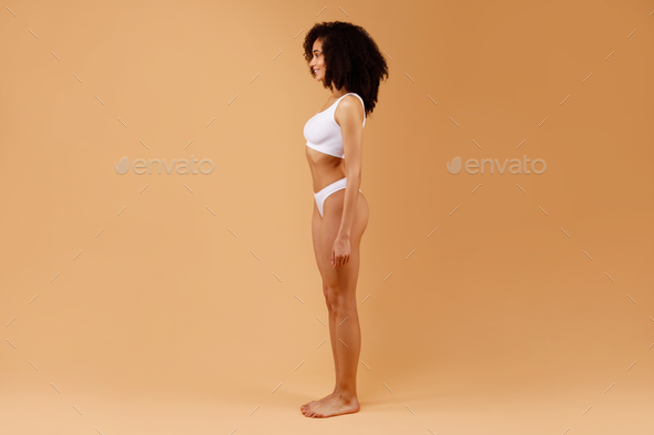 Side view of slim lady in white underwear posing isolated on beige