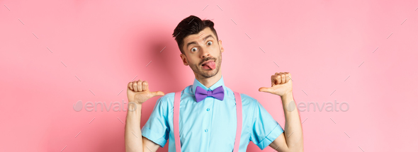 Funny guy in suspenders and bow-tie showing tongue, pointing at himself as if self-promoting