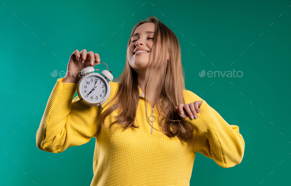 Smiling woman with alarm clock on teal studio.Early morning, correct day routine