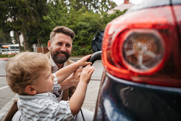 Close up of mature man and his little son charging their electric car on the street.