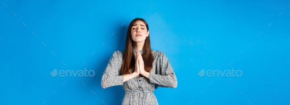 Pleading woman in dress begging for wish come true, supplicating god, standing against blue