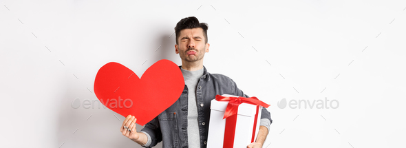 Sad and heartbroken man being rejected, crying and holding red heart with gift box, breakup on