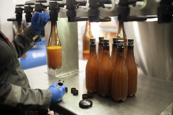 an employee on the factory filling new plastic bottle with beer from faucet