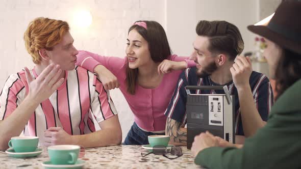 Portrait of Positive Young Woman Putting Hands on Shoulders of Men Sitting at Table on Vintage Cafe alt