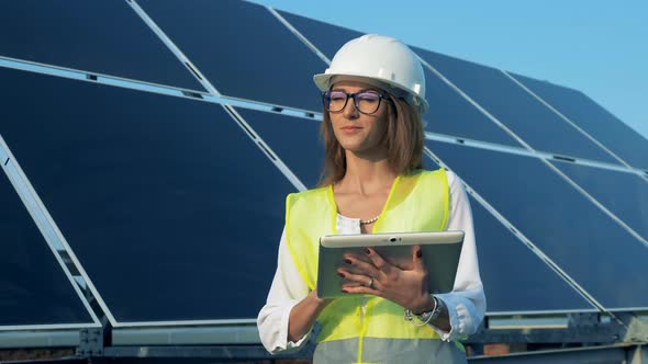Smiling Lady Expert Is Standing Near a Solar Battery with a Tablet alt