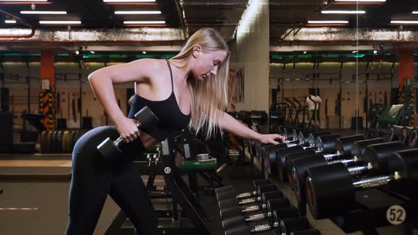 Young woman working hard in gym with dumbbell in front of the mirror to keep fit alt