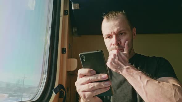 A Man on a Train at the Window Reads a Message on His Phone