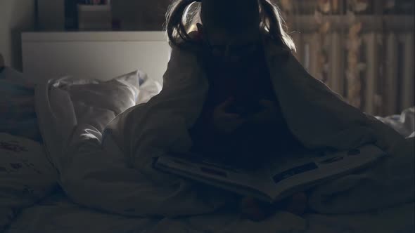A Young Girl Reading a Book Under the Covers with a Flashlight. RAW Video Record. alt