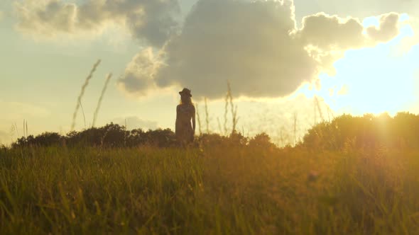 Young bohemian woman walking on a meadow during sunset