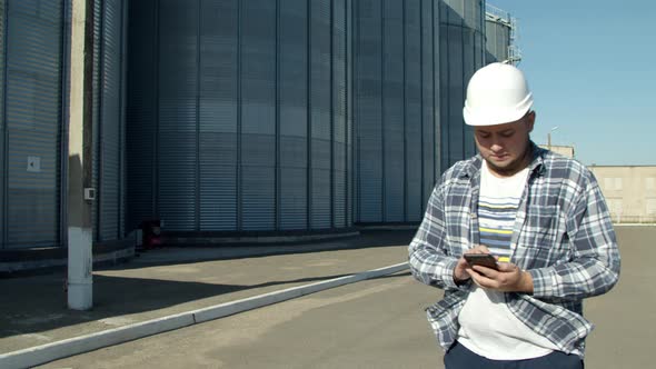 Professional Engineer Doing Calculations Near Agricultural Silos