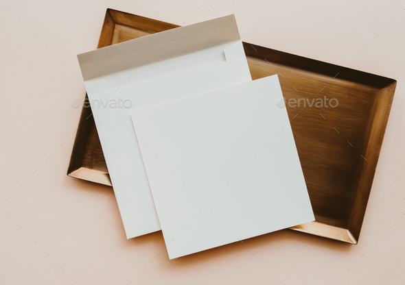 White blank paper square card mockup on gold tray on beige background.