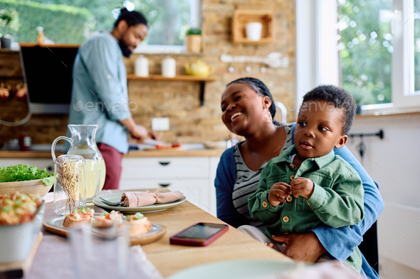 Little black boy sitting on mother's lap at dining table. Stock Photo ...