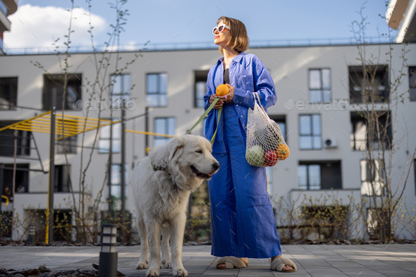 Woman carrying meshbag with fresh groceries while walking home with her dog