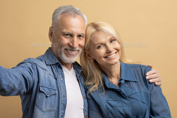 Cheerful beautiful elderly couple taking selfie, cuddling on