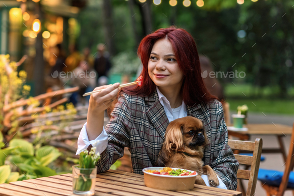 A woman with dog eating a poke in a park