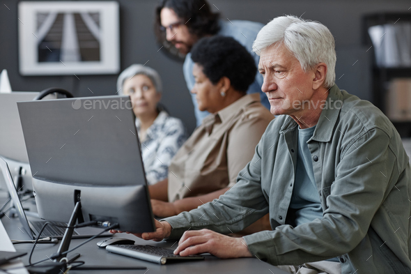 White haired senior man using computer in tech school for elderly people
