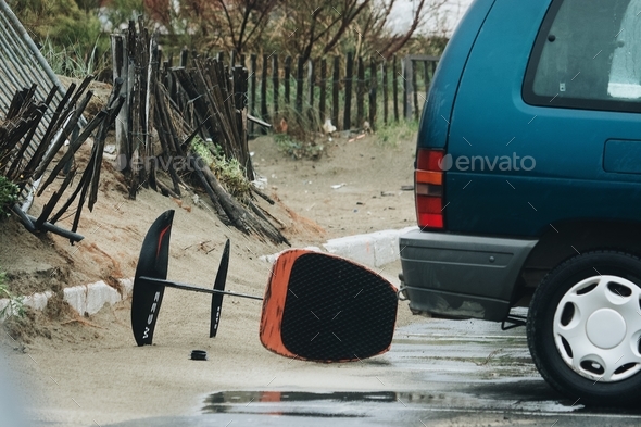 Rear of a green car with a chair that fell down and broken fences on a wet street