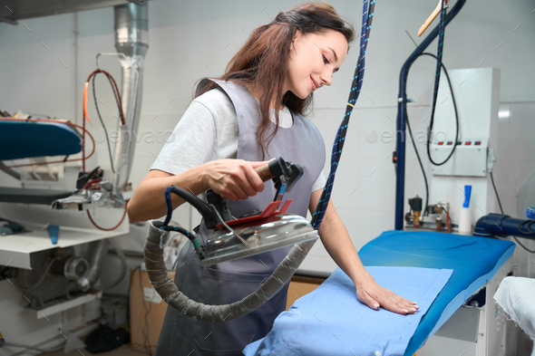 Woman laundry worker getting rid of wrinkles on shirt with hot industrial iron