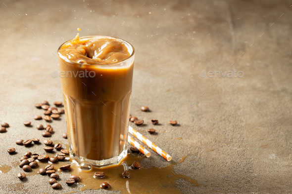 Splash of iced coffee in tall glass and coffee beans. Stock Photo