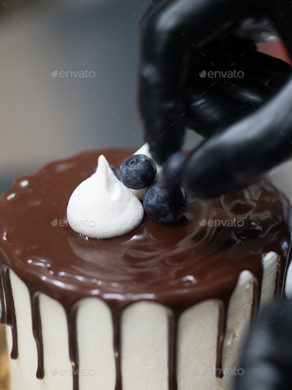 cake designer decorating a chocolate drip cake with mering and blueberries