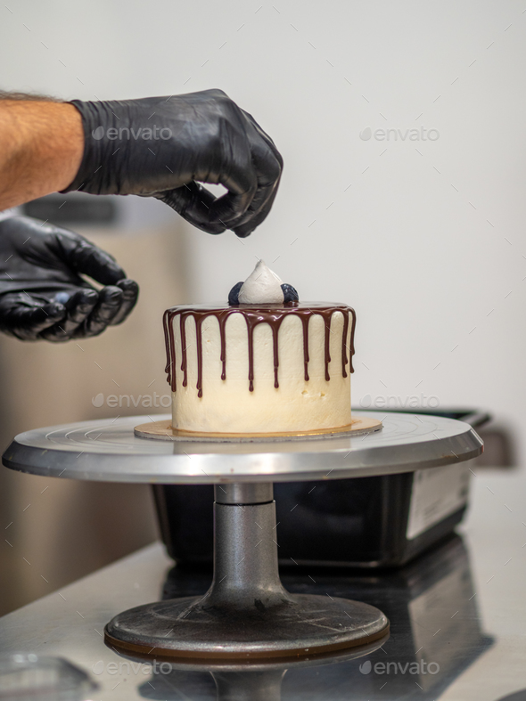 cake designer decorating a chocolate drip cake with meringue and blueberries