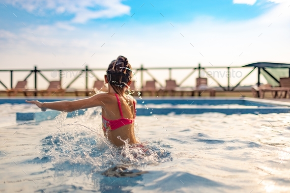 A girl in a bright bathing suit and glasses splashes clean water around  herself in the pool Stock Photo by YouraPechkin