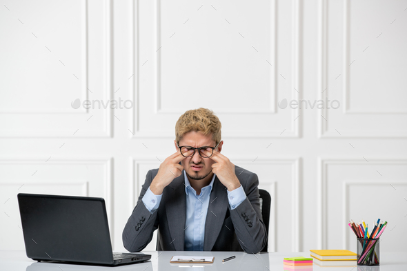 ADHD in the office young stressed worker in suit behind desk with computer scratching eyes