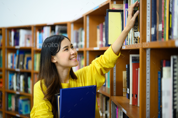 Asian female student picking up a book, choosing books from shelf in ...