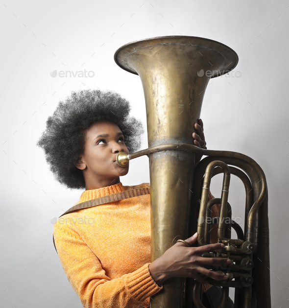 Portrait of a young black woman with short curly hair playing the tuba  Stock Photo by wirestock