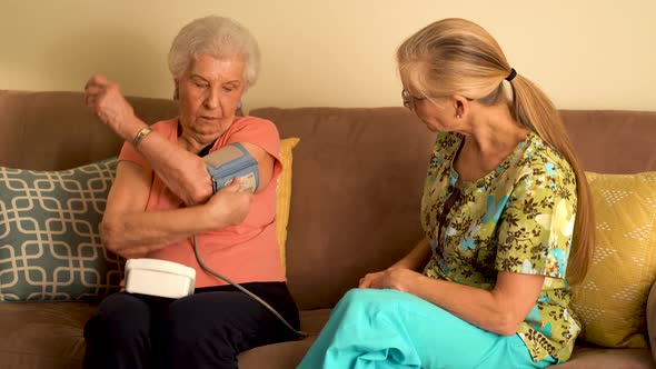 Home healthcare nurse and elderly woman taking blood pressure with a monitor. alt