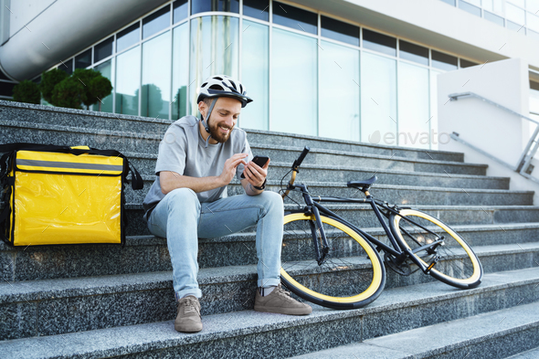 Express food delivery courier sitting on the stairs with insulated bag and bicycle.