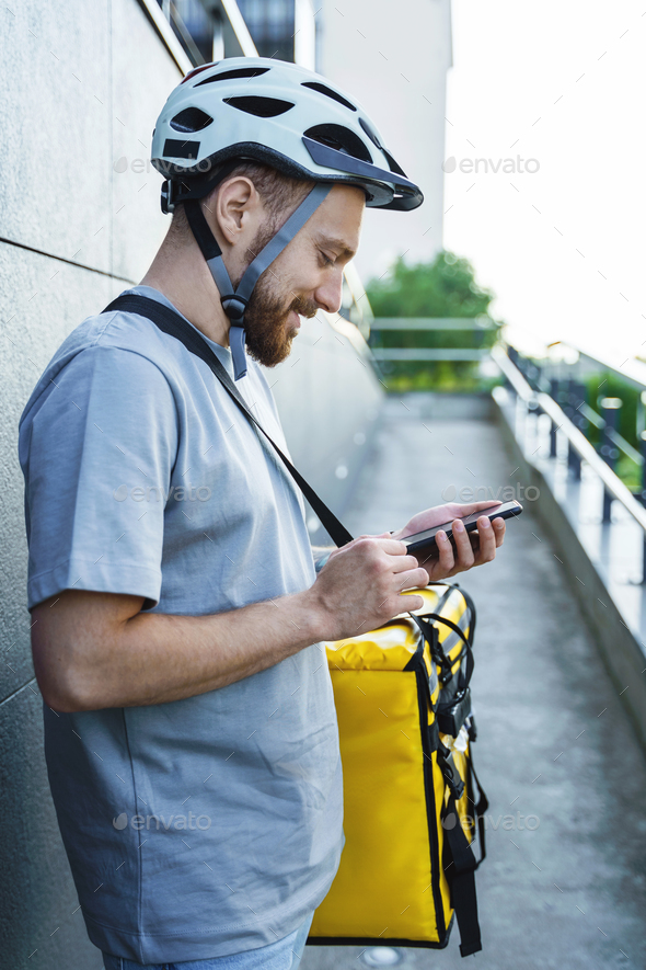 Express food delivery courier with insulated bag looking at phone.