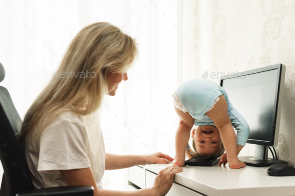 Little boy standing upside down on a desk and distracting mother from work on computer.