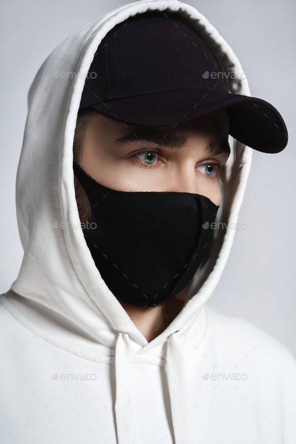 Man wearing white hoodie, black baseball cap and cloth face mask