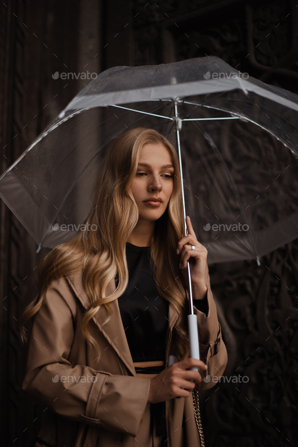 young woman holding transparent umbrella. Urban solitude in rain. Woman seeking shelter from rain