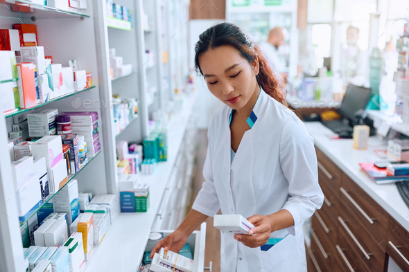 Female Chinese female pharmacist looking for medicine while working in drugstore.