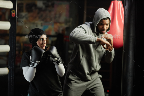 Young serioua Muslim sportswoman in boxing gloves crossing arms