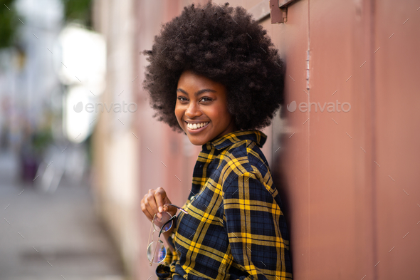 Beautiful young african woman with afro hair leaning against wall and ...