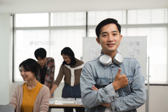 Portrait of relaxed man creative designer standing in office with colleagues meeting in background