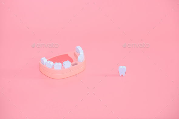 Teeth loss concept. Wooden jaw model with missing or extracted tooth with sad emoji on pink backgrou