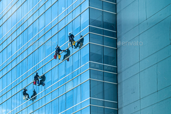 Group of cleaners in safety harness cleaning glass windows of a modern