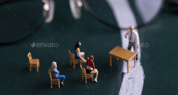 Closeup of tiny figures of a professor in front of the desk and students sitting - school concept