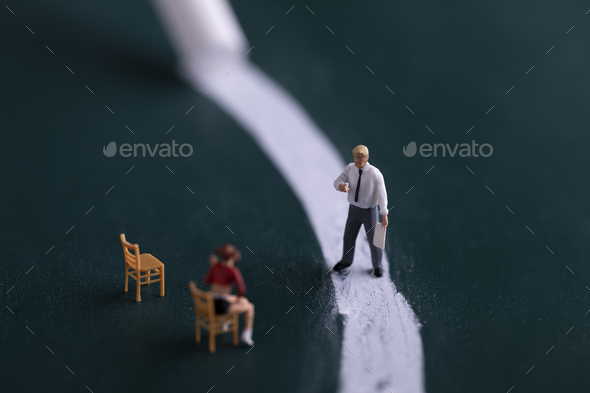 Closeup of tiny figures of a professor standing in front and a student sitting - school concept