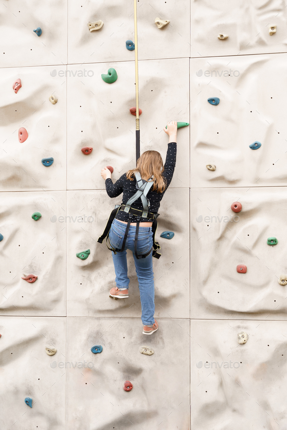 Teenage teen girl grabbing artificial high climbing wall with split ...